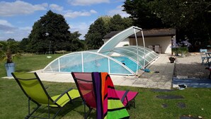 Una piscina cubierta con techo transparente, rodeada de césped y árboles.