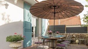 An outdoor patio with a table set for dining, surrounded by chairs, and an umbrella providing shade.