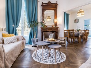 A living room with a sofa, a coffee table, a dining table with chairs, a large mirror, and a potted plant. - Charming 20th-Century House, 8 Bikes, Garden, Ping-Pong, Near Amenities (Bouvron)