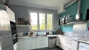 A modern kitchen with white cabinets, a stainless steel dishwasher, a built-in oven, and a window providing natural light.