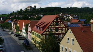 A row of traditional half-timbered houses with red-tiled roofs, a cobblestone street, and a hill with a castle in the background. - Gasthaus Schwarzer Adler (Colmberg)