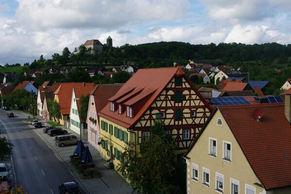 A row of traditional half-timbered houses with red-tiled roofs, a cobblestone street, and a hill with a castle in the background. - Gasthaus Schwarzer Adler (Colmberg)