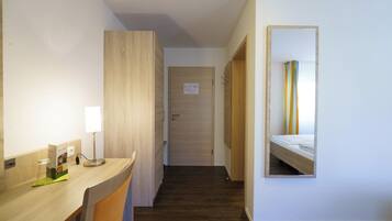 A hotel room with a wooden desk, a mirror, a bed, and a door.