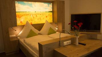 Un dormitorio moderno con un cuadro grande de un campo, cabecero de madera, mesita de noche con un florero y televisor.