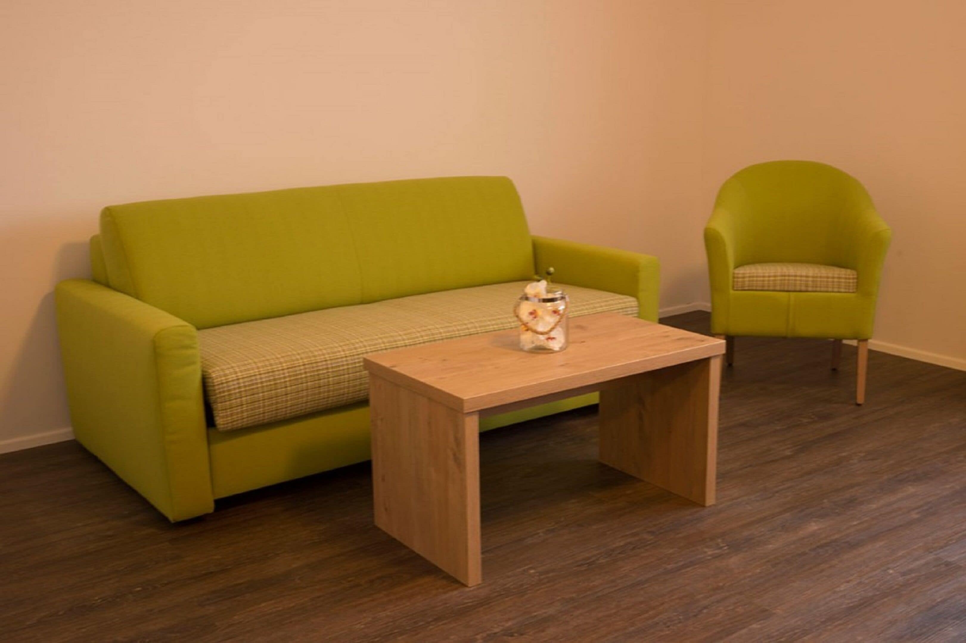 A room with a green sofa, a matching armchair, and a wooden coffee table with a decorative item on it.