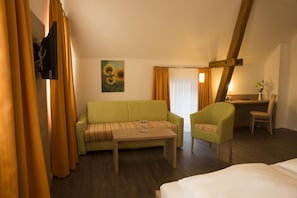 A hotel room with a green sofa, a wooden coffee table, a green armchair, a desk with a chair, and a bed. - Gasthaus Schwarzer Adler (Colmberg)