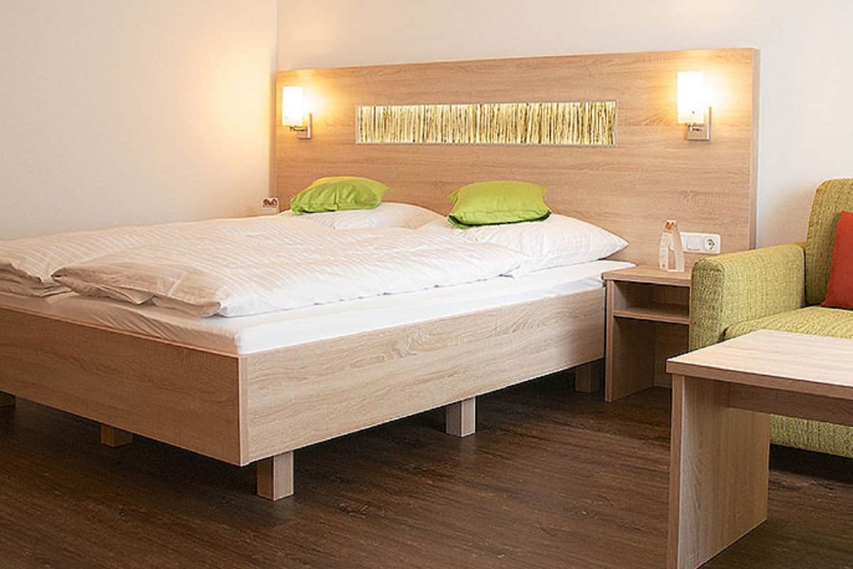 A modern hotel room with a wooden bed, green pillows, a nightstand, and a small table.