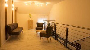 A modern living room with a sofa, two armchairs, a coffee table, and a staircase with a railing. - Gasthaus Schwarzer Adler (Colmberg)