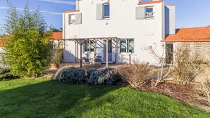 A two-story house with a covered patio area, a small garden, and a clear blue sky. - Charming Cottage near Pornic, 5km from Beach, Garden, WiFi, Family-Friendly (Pornic-Le Clion sur Mer)