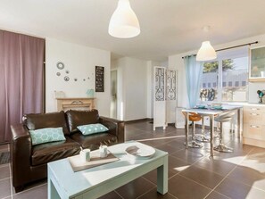 Ein modernes Wohnzimmer mit einem braunen Ledersofa, einem hellblauen Couchtisch und einem Essbereich mit einem weißen Tisch und Metallstühlen.