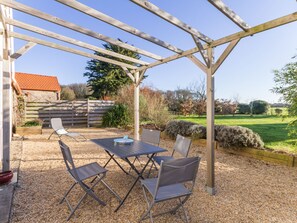 A covered patio with a table and chairs, a wooden pergola, and a view of a garden and house in the background. - Charming Cottage near Pornic, 5km from Beach, Garden, WiFi, Family-Friendly (Pornic-Le Clion sur Mer)