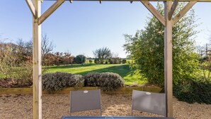 A wooden pergola with a table and chairs in a garden. - Charming Cottage near Pornic, 5km from Beach, Garden, WiFi, Family-Friendly (Pornic-Le Clion sur Mer)