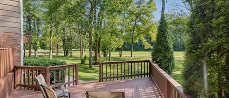 A wooden deck with chairs and a view of a green landscape.