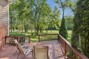A wooden deck with chairs and a table, overlooking a well-maintained lawn and trees.