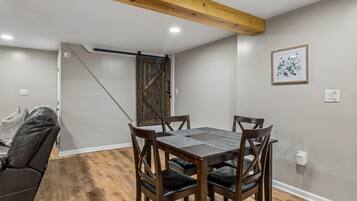 Un comedor con mesa y sillas de madera, techo con vigas a la vista y puerta que da a otra habitación.