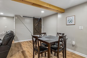 A dining area with a wooden table and chairs, a ceiling with exposed beams, and a door leading to another room.