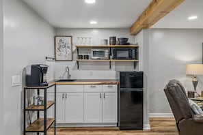 A compact kitchen with white cabinets, a black refrigerator, and a microwave on a shelf.