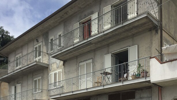 A multi-story building with balconies, some with metal railings and others with wooden shutters.