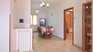 A dining area with a table set for four, a refrigerator, a clock, and a cabinet with glassware.