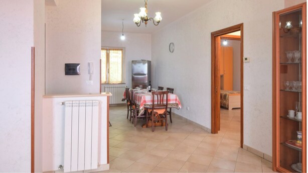 A dining area with a table set for four, a refrigerator, a clock, and a cabinet with glassware.