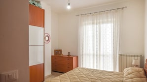 A bedroom with a bed, a dresser, a wardrobe, a window with curtains, and a radiator.