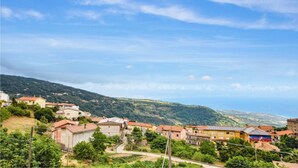 A hillside village with traditional buildings, a clear sky, and a view of the distant mountains.