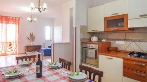 A dining area with a table set for four, a bottle of wine, and a chandelier. There is a kitchen area with a stove, oven, and microwave.