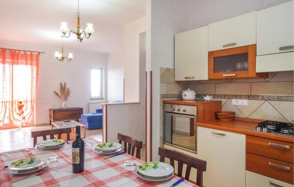 A dining area with a table set for four, a bottle of wine, and a chandelier. There is a kitchen area with a stove, oven, and microwave. - Apartment in Falerna 100sqm with Panoramic Gulf View, Free WiFi + SmartTv (Falerna)