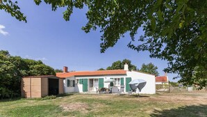 Een gelijkvloers huis met een rode dakbedekking, een kleine aangebouwde garage en een terras met tuinmeubilair.