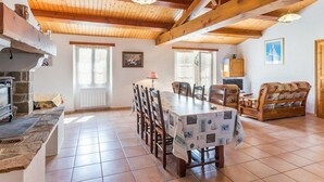 Een ruime woonkamer met houten plafond, een eettafel met stoelen, een bank en een open haard.