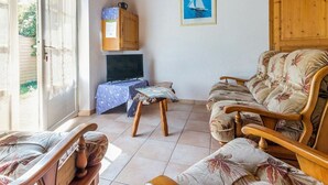 Een gezellige woonkamer met een houten plafond, een bank, een fauteuil, een kleine tafel en een televisie.