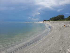 A beach with clear water, pebbles, and a few people.