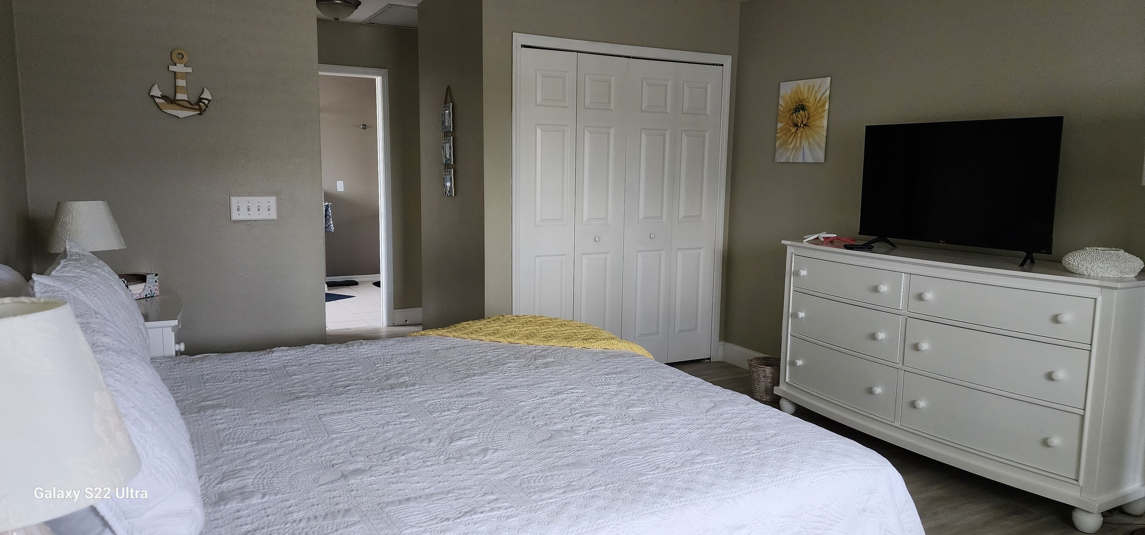 A bedroom with a bed, a dresser, a television, and a door leading to another room.
