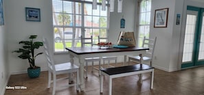 Een eethoek met een tafel, stoelen, een potplant en een tas met een strandthema.