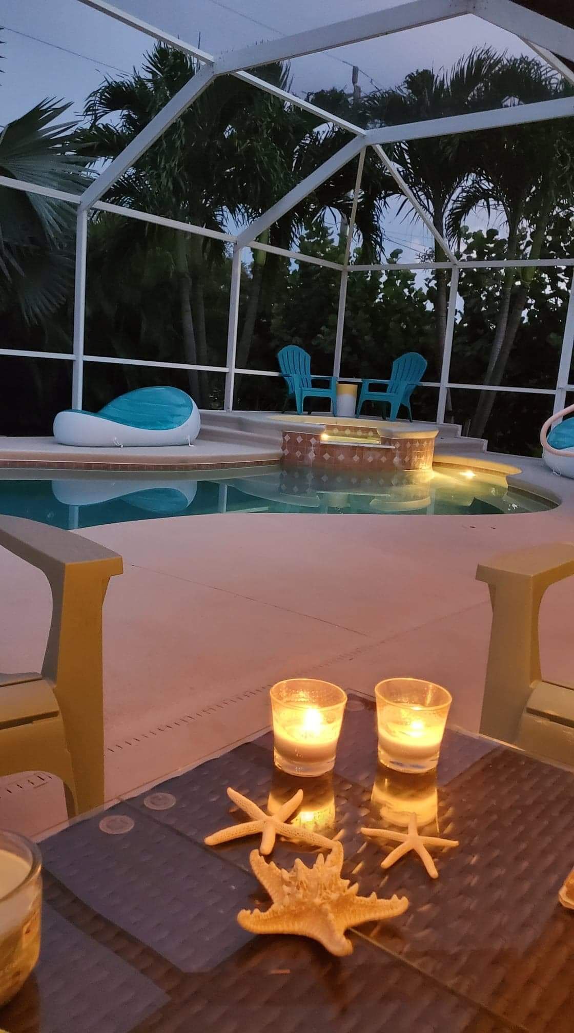 An outdoor pool area with a covered seating area, two candles on a table, and starfish decorations.