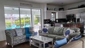 A spacious living area with a large sliding glass door leading to a pool, a kitchen with white cabinets, and a dining area with a bar. - Privacy in Paradise (CapeCoral)