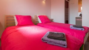 Ein Schlafzimmer mit zwei Betten, jeweils mit Holz Kopfteil und rosa Bettwäsche. Auf den Betten liegen gestapelte Handtücher.
