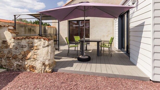 Eine Terrasse im Freien mit Tisch und Stühlen, einem violetten Sonnenschirm und einer Steinmauer.