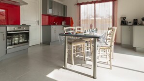 Eine moderne Küche mit Essbereich, ausgestattet mit einer Edelstahl-Dunstabzugshaube, grauen Schränken und einer roten Rückwand.