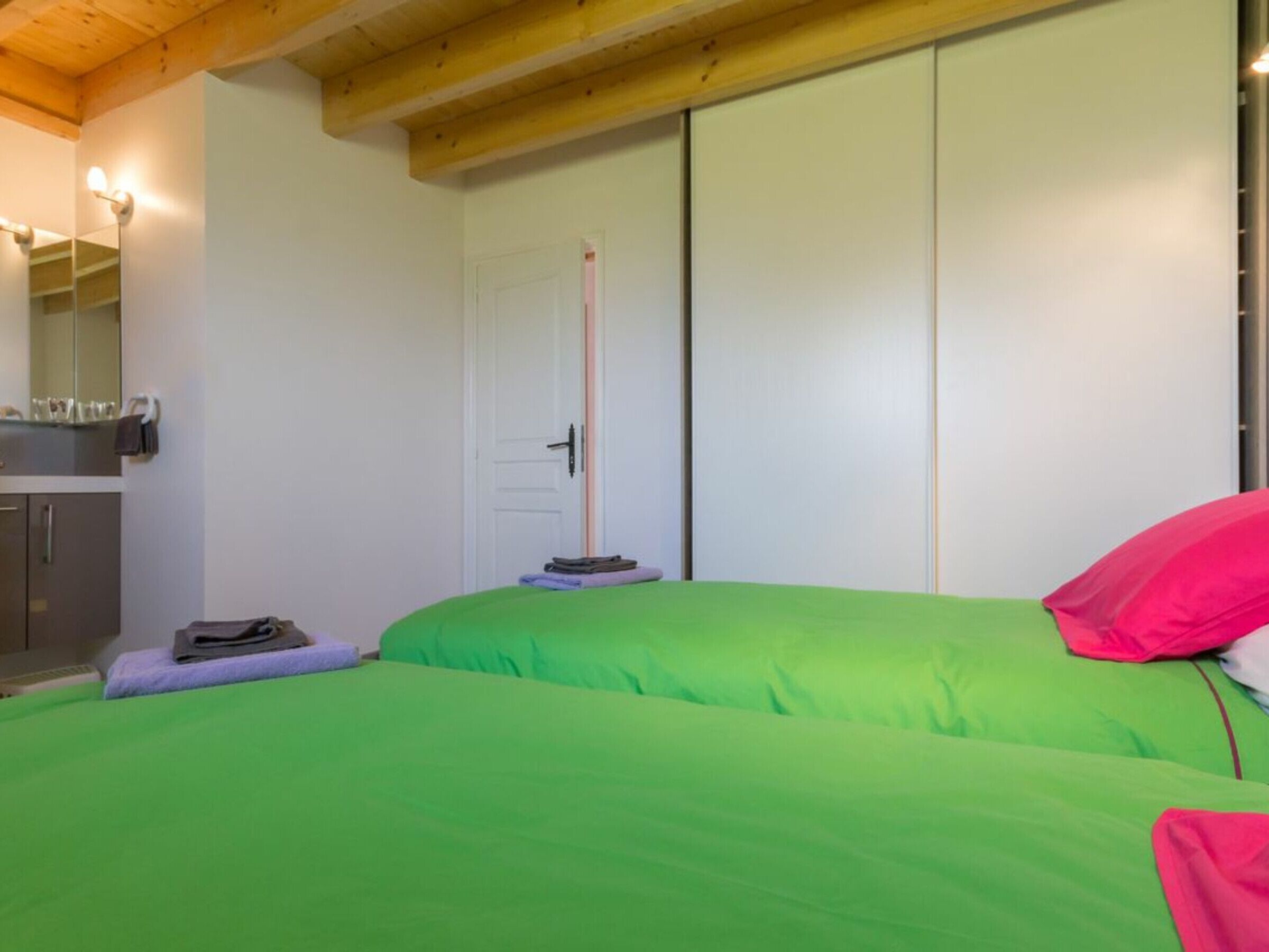 A bedroom with two beds, a wooden ceiling, a white door, and a small table with a mirror.