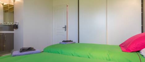 A bedroom with two beds, a wooden ceiling, a white door, and a small table with a mirror.