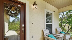 A front door with a wreath, a porch with two wooden chairs and a table, and a wall-mounted light fixture. - Biloxi Waterfront House With A View / Downtown Biloxi, Ocean Springs & Keesler (Biloxi)