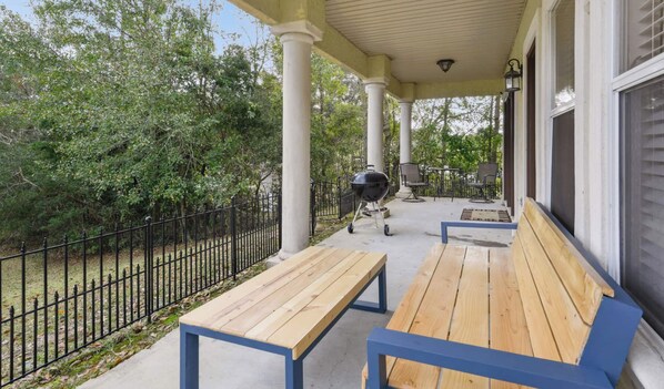 Une terrasse extérieure avec deux bancs en bois, un barbecue et une clôture en métal noir.