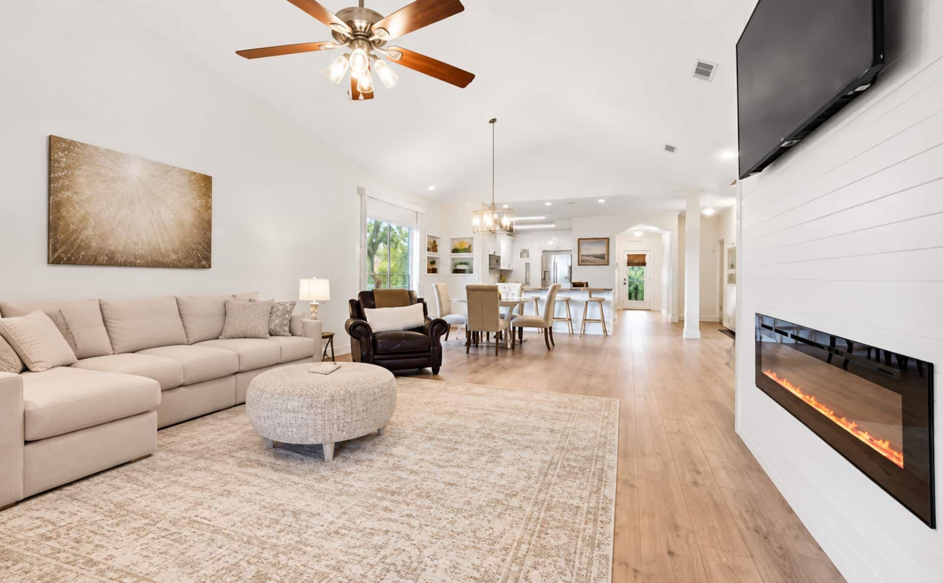 A modern living room with a sectional sofa, a round ottoman, a ceiling fan, and a fireplace.