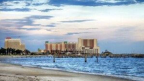 A coastal cityscape with high-rise buildings, a beach, and a pier extending into the water.