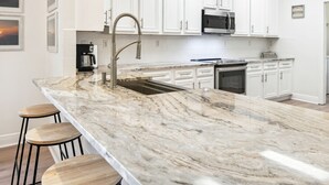 A modern kitchen with white cabinetry, a marble countertop, and a stainless steel sink.