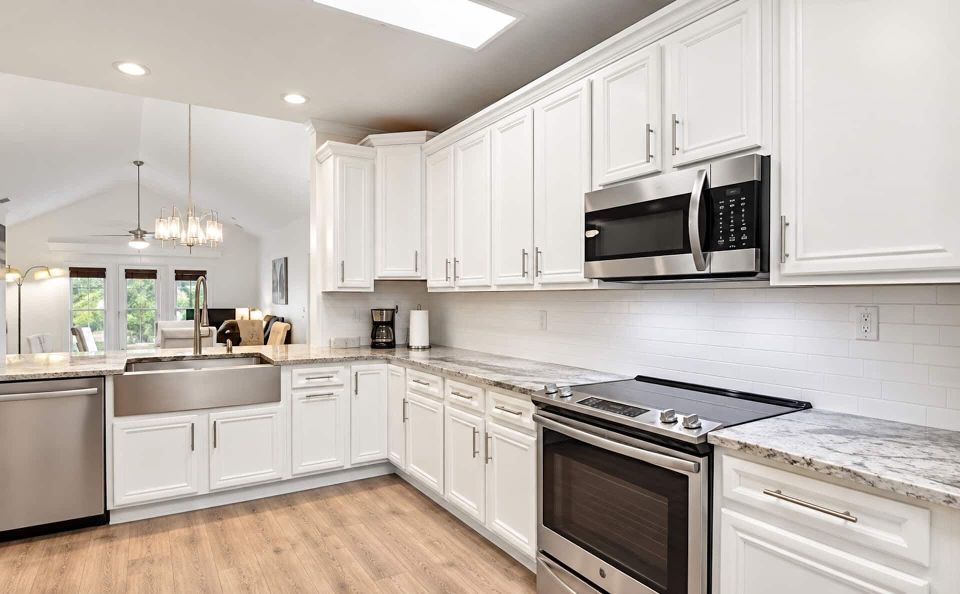 Cocina moderna con armarios blancos, electrodomésticos de acero inoxidable y encimera de mármol.