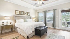 A bedroom with a large bed, a nightstand, a ceiling fan, and a view through a sliding glass door. - Biloxi Waterfront House With A View / Downtown Biloxi, Ocean Springs & Keesler (Biloxi)
