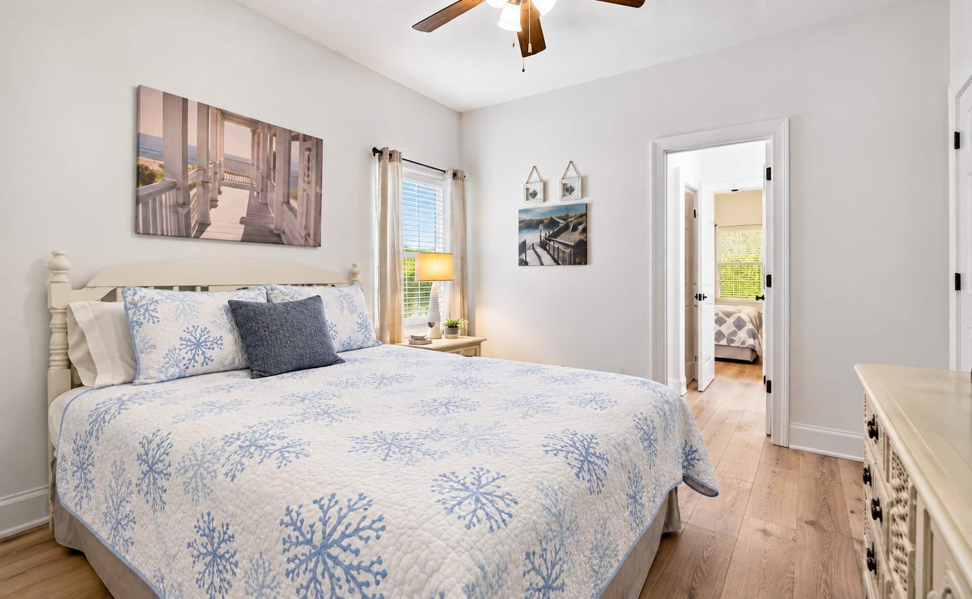 A bedroom with a bed, a nightstand, a ceiling fan, and a door leading to another room.