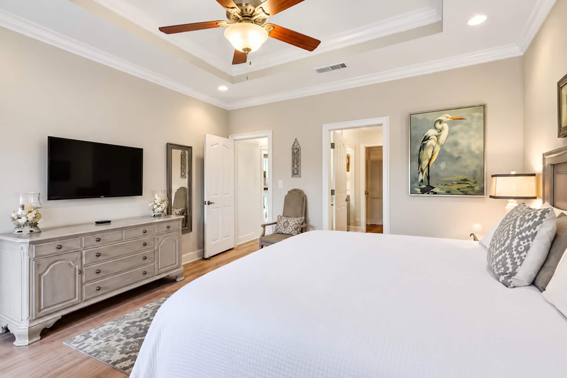 Spacious, elegant bedroom with TV, tray ceiling, and serene decor